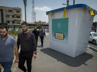 Iranian men are walking past a model of a ballot box that is being placed street-side in downtown Tehran, Iran, on June 14, 2024, during Ira...