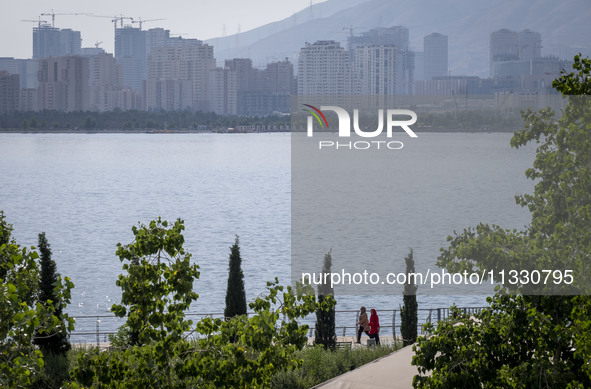 Two Iranian women are walking along a recreation area in western Tehran, Iran, on June 14, 2024, amidst the early presidential election camp...