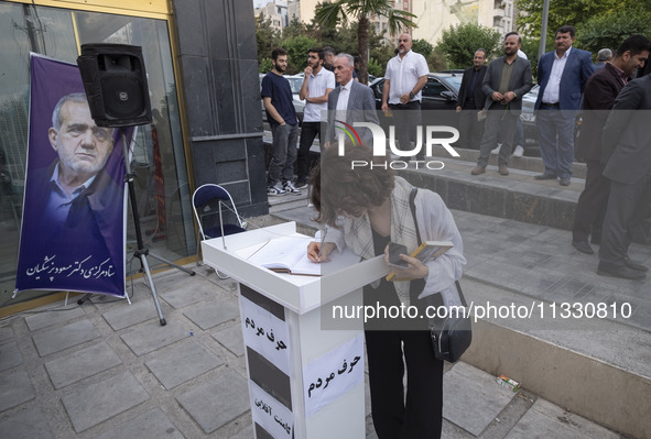 A young Iranian woman, who is not wearing a mandatory headscarf, is writing a note in a notebook dedicated to Masoud Pezeshkian, a reformist...