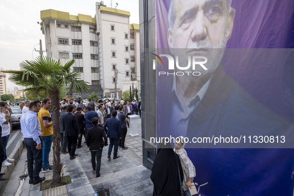 Two young women are walking past a banner featuring a portrait of Masoud Pezeshkian, a reformist presidential candidate, during an electoral...