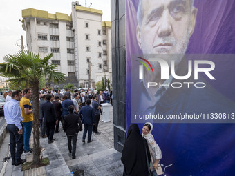 Two young women are walking past a banner featuring a portrait of Masoud Pezeshkian, a reformist presidential candidate, during an electoral...