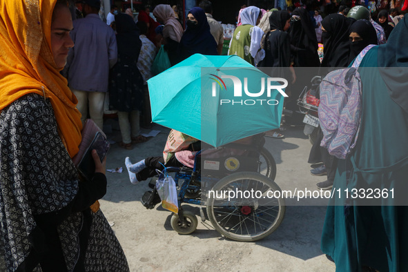 A woman in a wheelchair is holding an umbrella as she shops at a market ahead of the Eid al-Adha festival in Srinagar, India, on June 15, 20...