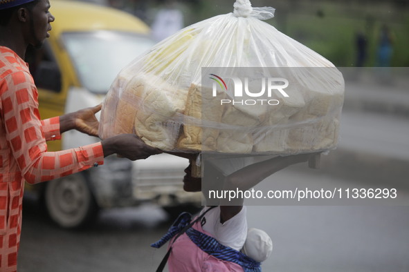 A man who is wanting to buy bread is helping a vendor drop a load of loaves off her head as Muslim faithful are praying to mark the Eid-El-K...