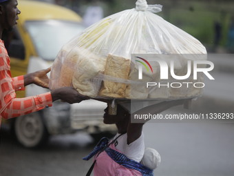 A man who is wanting to buy bread is helping a vendor drop a load of loaves off her head as Muslim faithful are praying to mark the Eid-El-K...