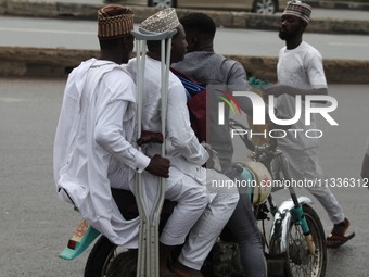 A commercial motorcyclist is carrying passengers as Muslim faithful are praying to mark the Eid-El-Kabir festival in Ikeja, Lagos, Nigeria,...