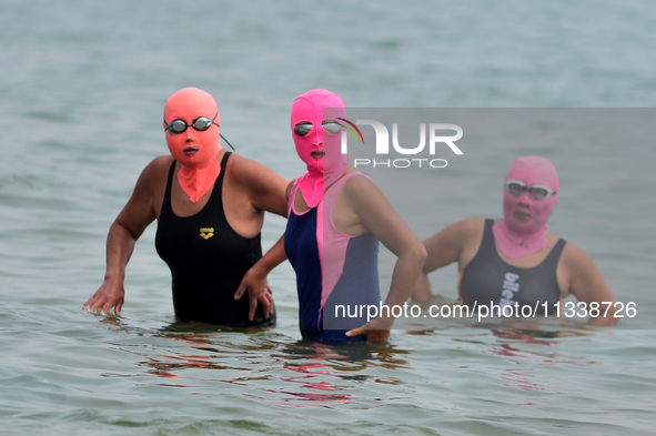 Three people are wearing face-kinis to cool off in the water at the No. 1 Bathing Beach in Qingdao, China, on June 17, 2024. 