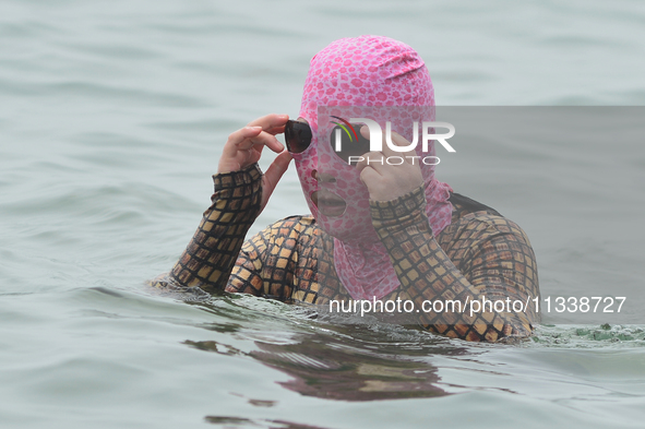 A citizen is wearing a face-kini with sun protection and cooling off in the water at the No. 1 Bathing Beach in Qingdao, China, on June 17,...