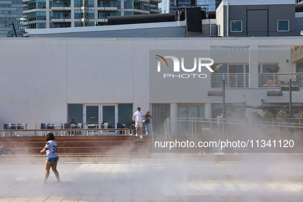 People are cooling off during a hot summer afternoon as they walk amongst water vapor being sprayed from the ground in Toronto, Ontario, Can...