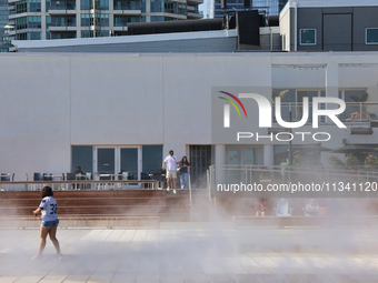 People are cooling off during a hot summer afternoon as they walk amongst water vapor being sprayed from the ground in Toronto, Ontario, Can...