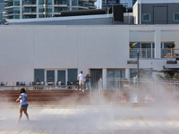 People are cooling off during a hot summer afternoon as they walk amongst water vapor being sprayed from the ground in Toronto, Ontario, Can...