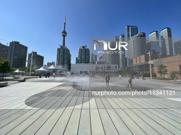 People are cooling off during a hot summer afternoon as they walk amongst water vapor being sprayed from the ground in Toronto, Ontario, Can...