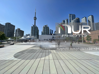 People are cooling off during a hot summer afternoon as they walk amongst water vapor being sprayed from the ground in Toronto, Ontario, Can...