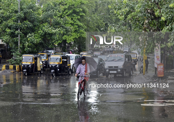 A Hindu priest is riding a bicycle and carrying an umbrella during rainfall in Mumbai, India, on June 18, 2024. 