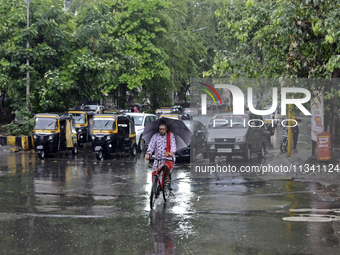 A Hindu priest is riding a bicycle and carrying an umbrella during rainfall in Mumbai, India, on June 18, 2024. (