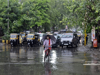 A Hindu priest is riding a bicycle and carrying an umbrella during rainfall in Mumbai, India, on June 18, 2024. (