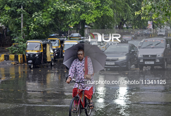 A Hindu priest is riding a bicycle and carrying an umbrella during rainfall in Mumbai, India, on June 18, 2024. 