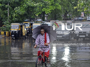 A Hindu priest is riding a bicycle and carrying an umbrella during rainfall in Mumbai, India, on June 18, 2024. (