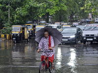 A Hindu priest is riding a bicycle and carrying an umbrella during rainfall in Mumbai, India, on June 18, 2024. (