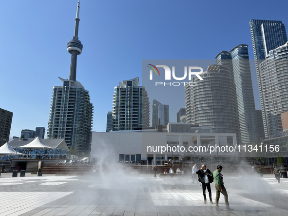 People are cooling off during a hot summer afternoon as they walk amongst water vapor being sprayed from the ground in Toronto, Ontario, Can...