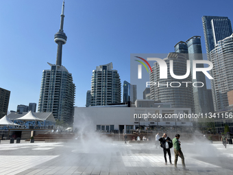 People are cooling off during a hot summer afternoon as they walk amongst water vapor being sprayed from the ground in Toronto, Ontario, Can...