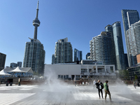 People are cooling off during a hot summer afternoon as they walk amongst water vapor being sprayed from the ground in Toronto, Ontario, Can...