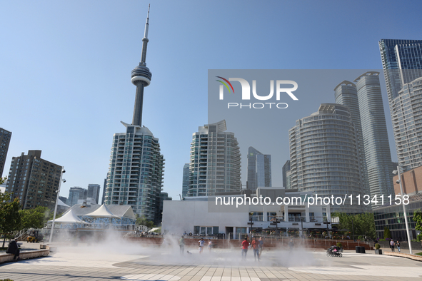 People are cooling off during a hot summer afternoon as they walk amongst water vapor being sprayed from the ground in Toronto, Ontario, Can...