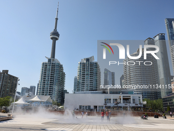 People are cooling off during a hot summer afternoon as they walk amongst water vapor being sprayed from the ground in Toronto, Ontario, Can...