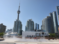 People are cooling off during a hot summer afternoon as they walk amongst water vapor being sprayed from the ground in Toronto, Ontario, Can...