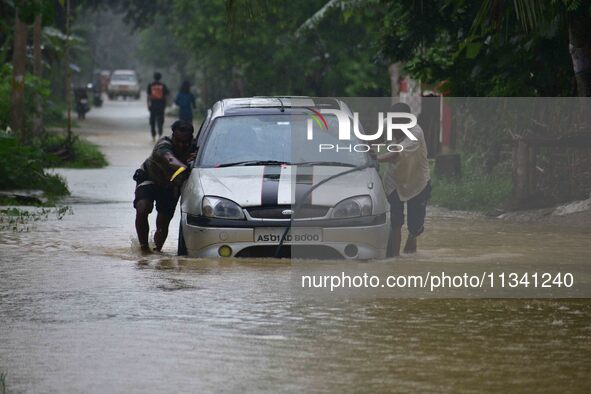 People are pushing a car through a flooded road following rains in Changchaki village in Nagaon District of Assam, India, on June 18, 2024. 