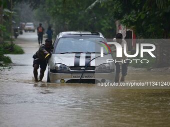 People are pushing a car through a flooded road following rains in Changchaki village in Nagaon District of Assam, India, on June 18, 2024....