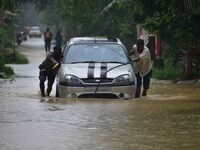 People are pushing a car through a flooded road following rains in Changchaki village in Nagaon District of Assam, India, on June 18, 2024....