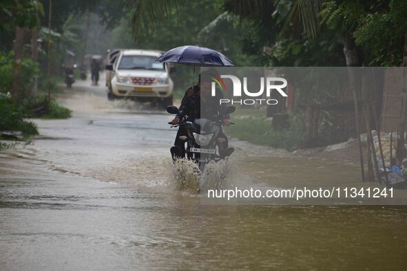 A man is riding his bike through a flooded road following rains in Changchaki village in Nagaon District of Assam, India, on June 18, 2024. 