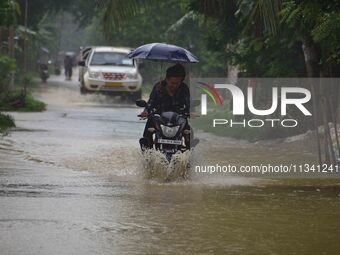 A man is riding his bike through a flooded road following rains in Changchaki village in Nagaon District of Assam, India, on June 18, 2024....