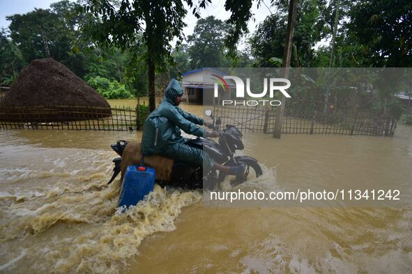 A man is riding his bike through a flooded road following rains in Changchaki village in Nagaon District of Assam, India, on June 18, 2024. 