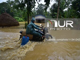 A man is riding his bike through a flooded road following rains in Changchaki village in Nagaon District of Assam, India, on June 18, 2024....