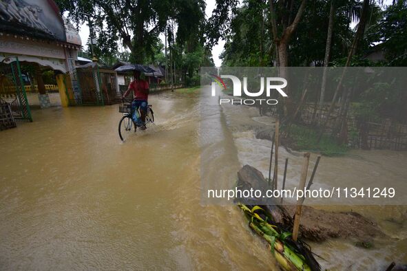 A man is riding his bicycle through a flooded road following rains in Changchaki village in Nagaon District of Assam, India, on June 18, 202...