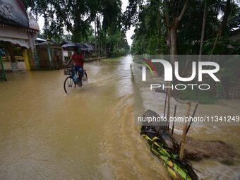 A man is riding his bicycle through a flooded road following rains in Changchaki village in Nagaon District of Assam, India, on June 18, 202...