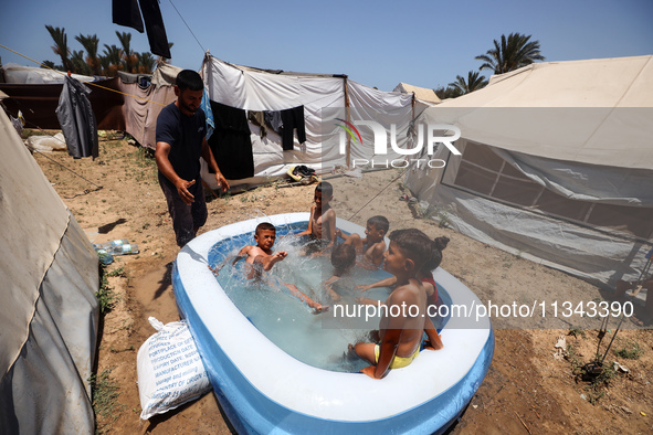 Palestinian children are playing with water outside their tent at a camp for displaced people, during a hot day in Deir al-Balah, in the cen...