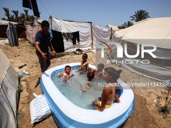 Palestinian children are playing with water outside their tent at a camp for displaced people, during a hot day in Deir al-Balah, in the cen...