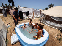 Palestinian children are playing with water outside their tent at a camp for displaced people, during a hot day in Deir al-Balah, in the cen...