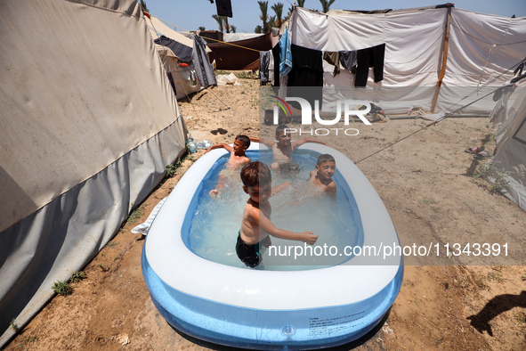 Palestinian children are playing with water outside their tent at a camp for displaced people, during a hot day in Deir al-Balah, in the cen...