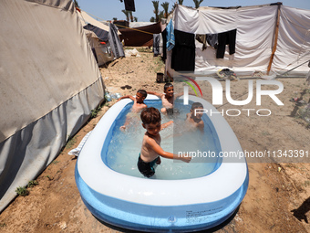 Palestinian children are playing with water outside their tent at a camp for displaced people, during a hot day in Deir al-Balah, in the cen...