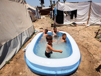 Palestinian children are playing with water outside their tent at a camp for displaced people, during a hot day in Deir al-Balah, in the cen...