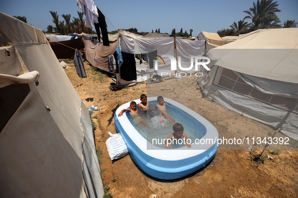 Palestinian children are playing with water outside their tent at a camp for displaced people, during a hot day in Deir al-Balah, in the cen...