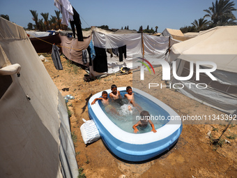 Palestinian children are playing with water outside their tent at a camp for displaced people, during a hot day in Deir al-Balah, in the cen...