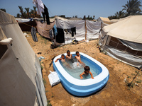 Palestinian children are playing with water outside their tent at a camp for displaced people, during a hot day in Deir al-Balah, in the cen...