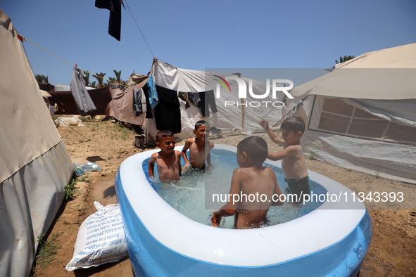 Palestinian children are playing with water outside their tent at a camp for displaced people, during a hot day in Deir al-Balah, in the cen...