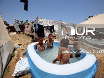 Palestinian children are playing with water outside their tent at a camp for displaced people, during a hot day in Deir al-Balah, in the cen...