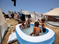 Palestinian children are playing with water outside their tent at a camp for displaced people, during a hot day in Deir al-Balah, in the cen...