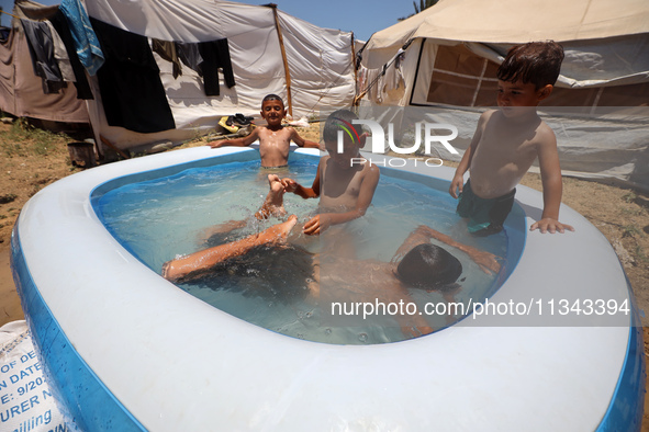 Palestinian children are playing with water outside their tent at a camp for displaced people, during a hot day in Deir al-Balah, in the cen...